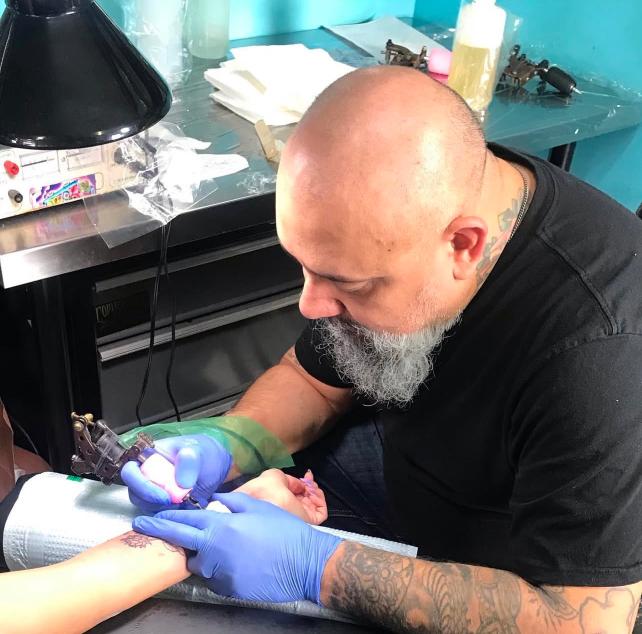 Julio Avila tattooing a woman's inner wrist in his shop